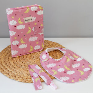 Canastilla artresanal para bebe con poortadocumentos, chupetero y babero. Con estampado de fondo rosa y dibujos de lunas y nubes